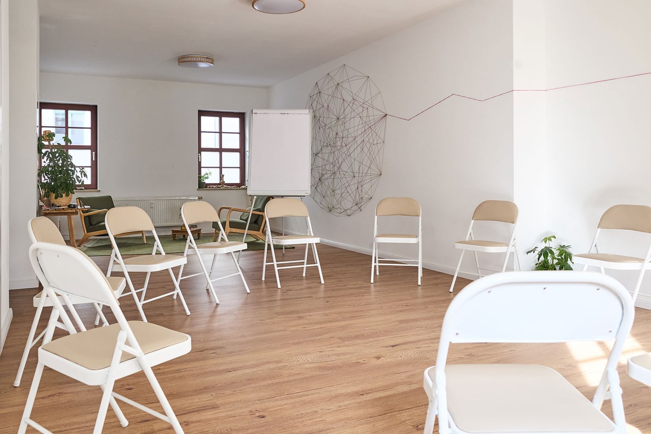 Heller Praxisraum mit einem Kreis aus Stühlen und einer Fadeninstallation an der Wand