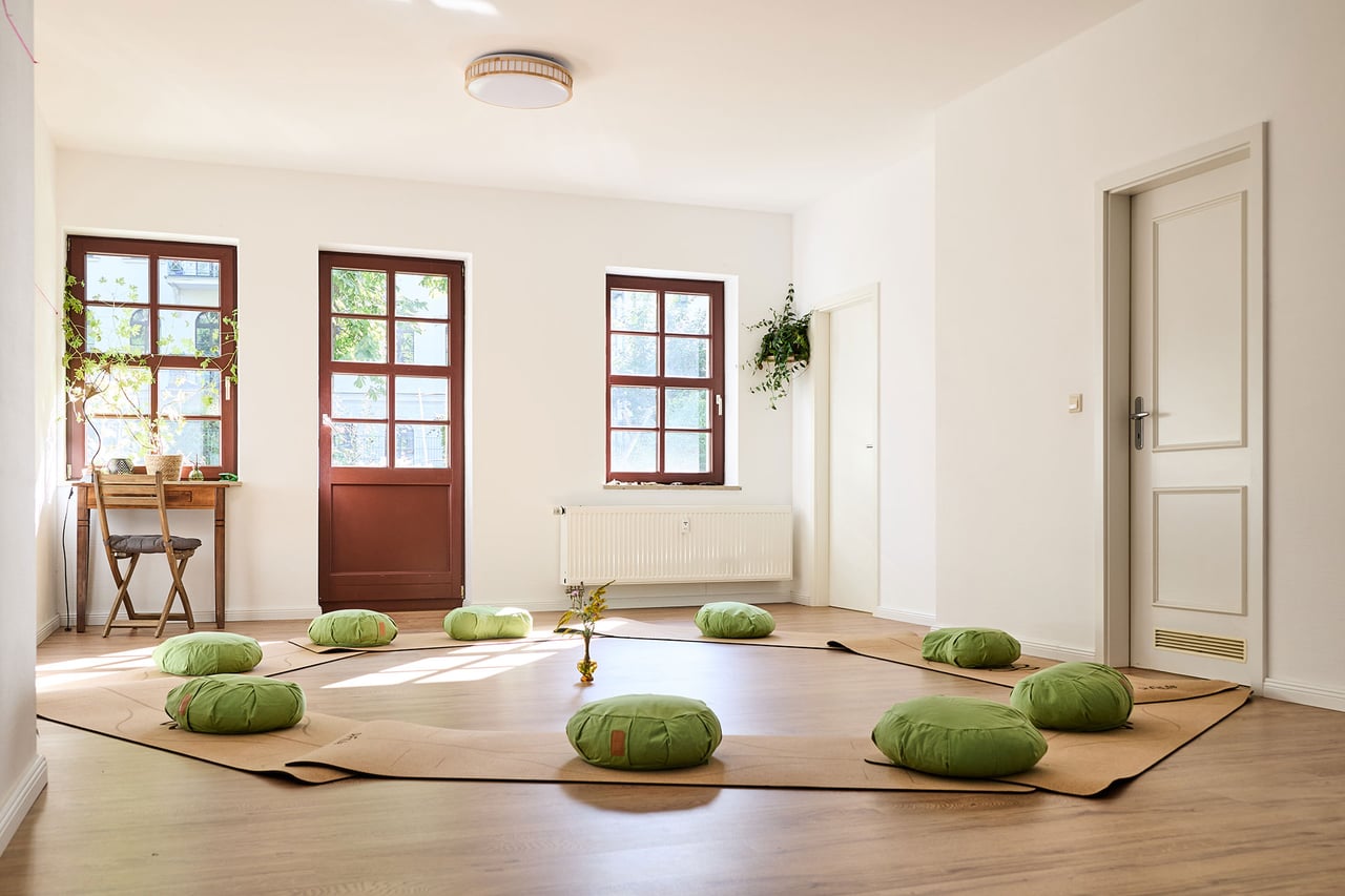 Grüne Meditationskissen auf Matten im Kreis vor den Fenstern